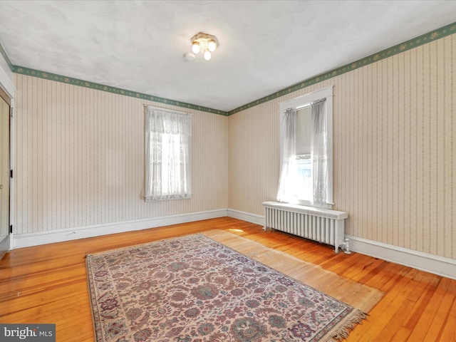 empty room featuring baseboards, wallpapered walls, wood-type flooring, and radiator