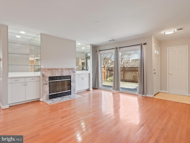 unfurnished living room with light wood-type flooring, a high end fireplace, visible vents, and recessed lighting