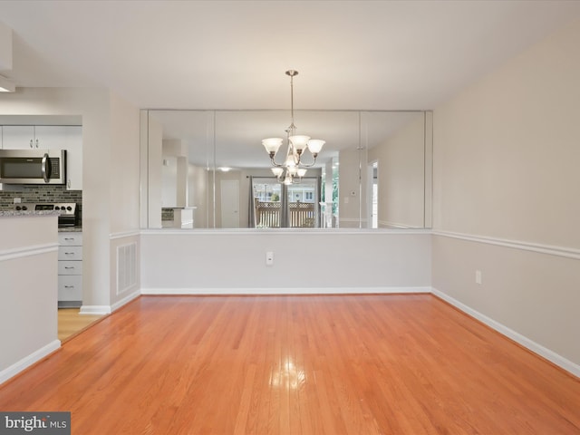 unfurnished dining area with a chandelier, visible vents, light wood-style flooring, and baseboards