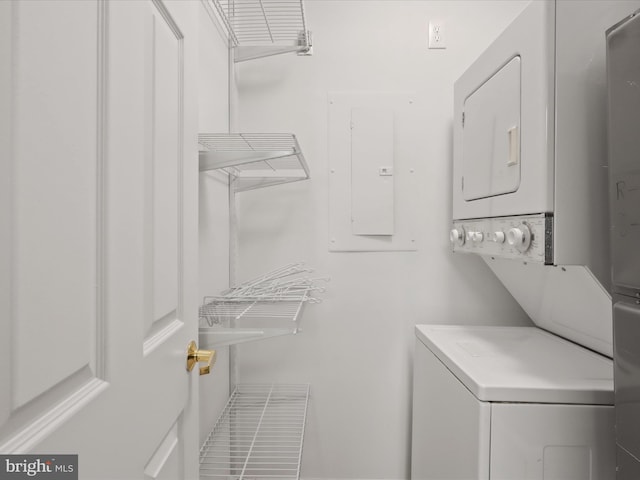 clothes washing area featuring laundry area, electric panel, and stacked washing maching and dryer