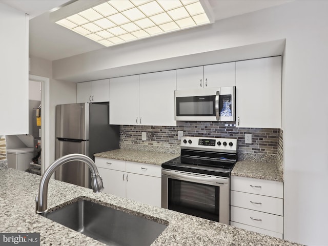 kitchen with appliances with stainless steel finishes, a sink, white cabinetry, and decorative backsplash