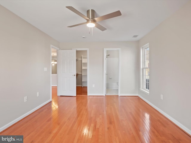 unfurnished bedroom with baseboards, ceiling fan, a walk in closet, light wood-style floors, and a closet