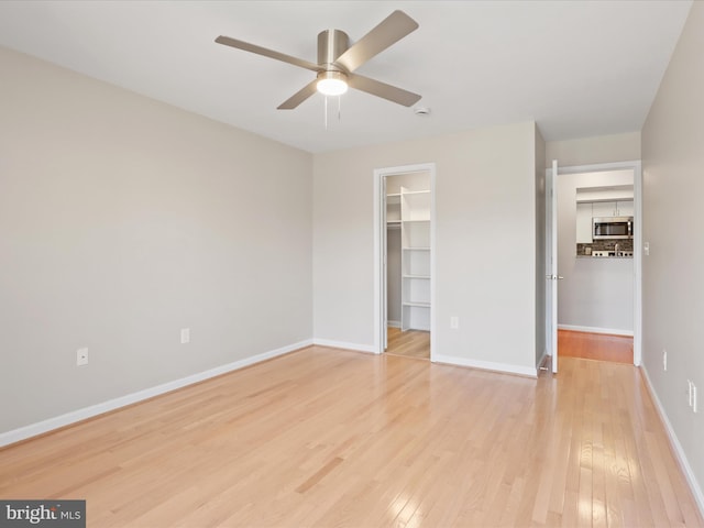 unfurnished bedroom with light wood finished floors, a closet, a spacious closet, ceiling fan, and baseboards