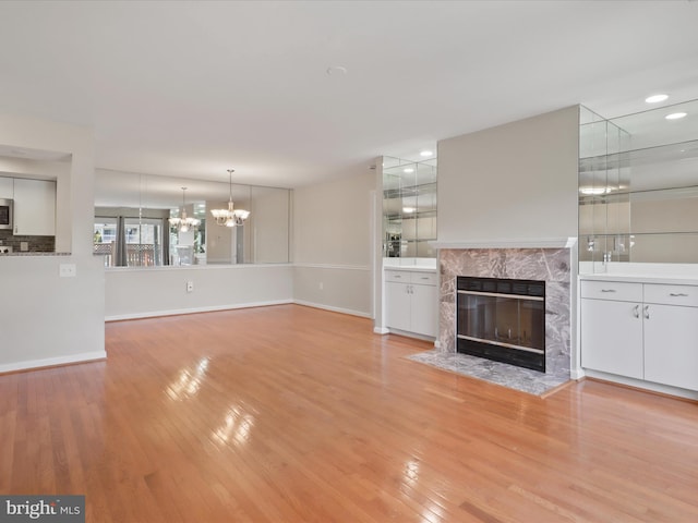 unfurnished living room featuring baseboards, light wood finished floors, a premium fireplace, and an inviting chandelier