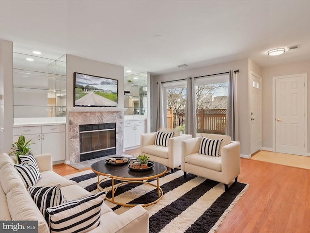 living area with a high end fireplace, visible vents, light wood finished floors, and recessed lighting