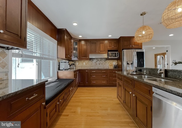 kitchen featuring light wood finished floors, decorative backsplash, appliances with stainless steel finishes, a sink, and under cabinet range hood