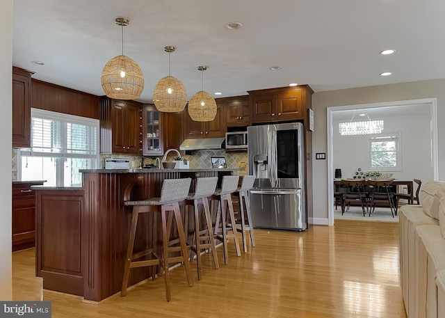 kitchen with appliances with stainless steel finishes, a kitchen bar, light wood-style flooring, and under cabinet range hood