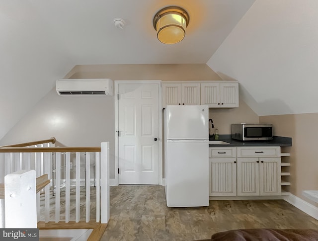 kitchen with dark countertops, stainless steel microwave, freestanding refrigerator, an AC wall unit, and a sink