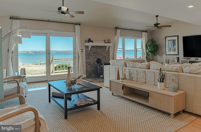 living room featuring ceiling fan, a water view, vaulted ceiling, light wood-style floors, and recessed lighting