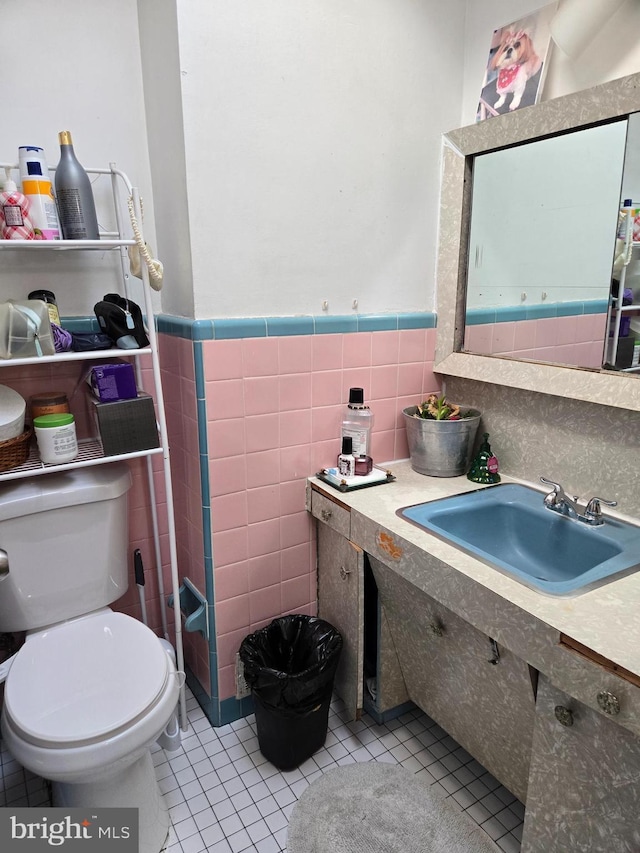 bathroom featuring wainscoting, toilet, a sink, tile patterned flooring, and tile walls