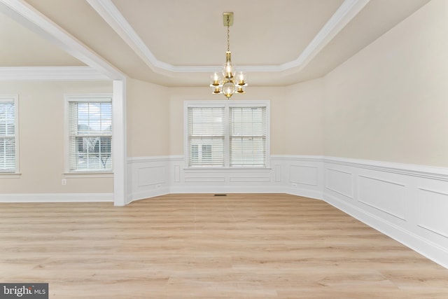 unfurnished dining area with light wood finished floors, a tray ceiling, wainscoting, crown molding, and a chandelier