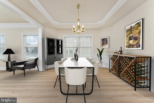 dining area featuring light wood-style floors, a raised ceiling, a notable chandelier, and crown molding