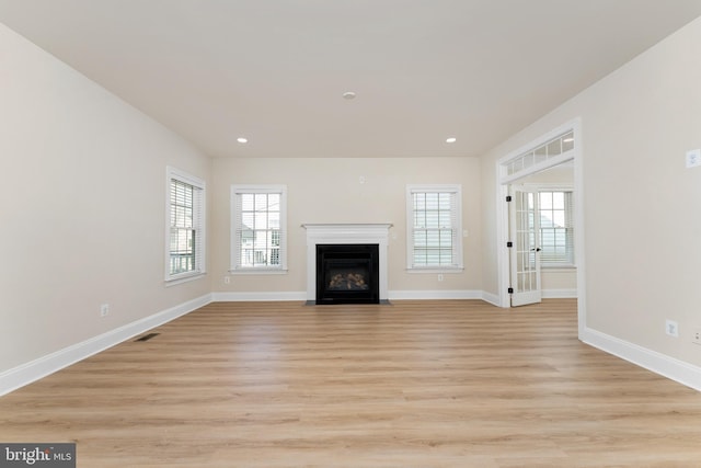 unfurnished living room with a fireplace with flush hearth, baseboards, and light wood finished floors