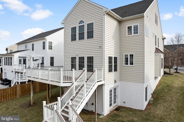 rear view of property featuring brick siding, fence, a wooden deck, stairs, and a lawn