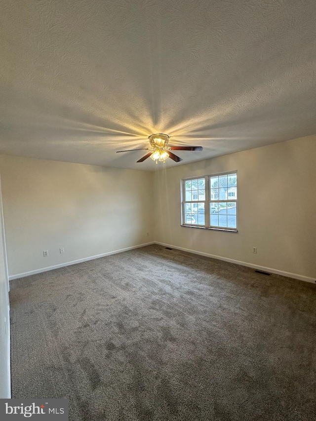 unfurnished room with baseboards, visible vents, dark carpet, and a textured ceiling