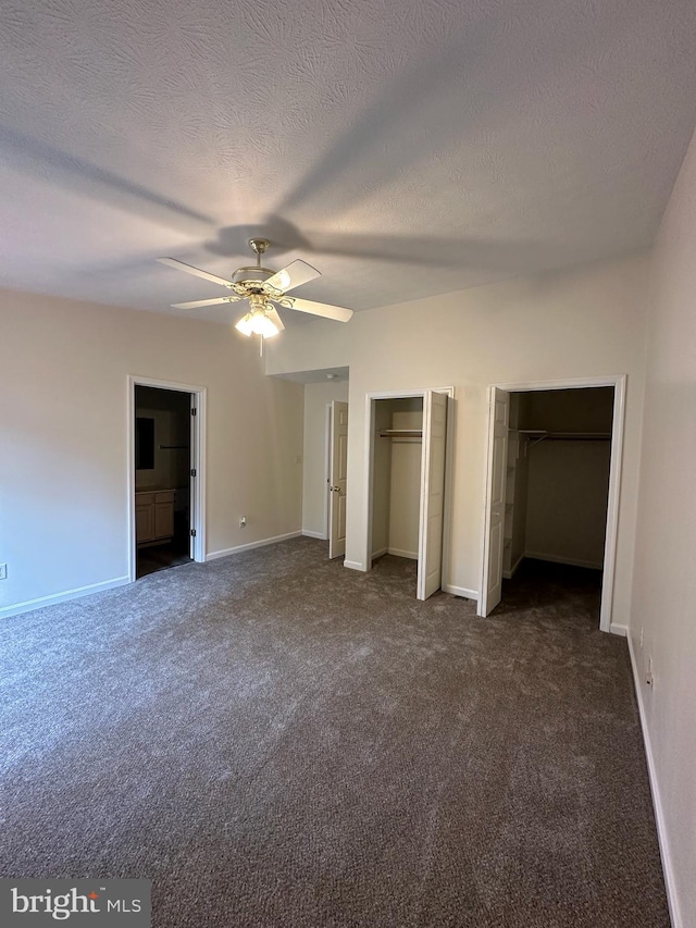 unfurnished bedroom featuring baseboards, dark carpet, and multiple closets