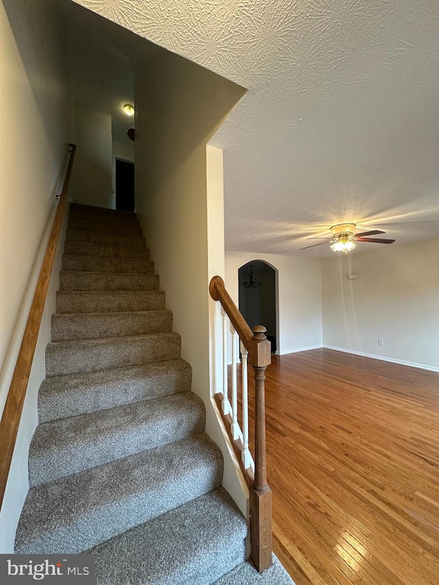 staircase with baseboards, arched walkways, ceiling fan, wood finished floors, and a textured ceiling