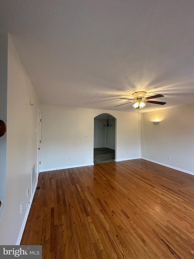 spare room featuring baseboards, arched walkways, a ceiling fan, wood finished floors, and a textured ceiling