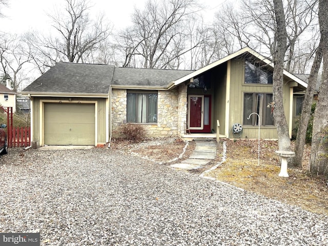 view of front facade featuring stone siding, an attached garage, gravel driveway, and roof with shingles