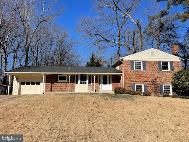 tri-level home featuring brick siding, a chimney, covered porch, a garage, and driveway