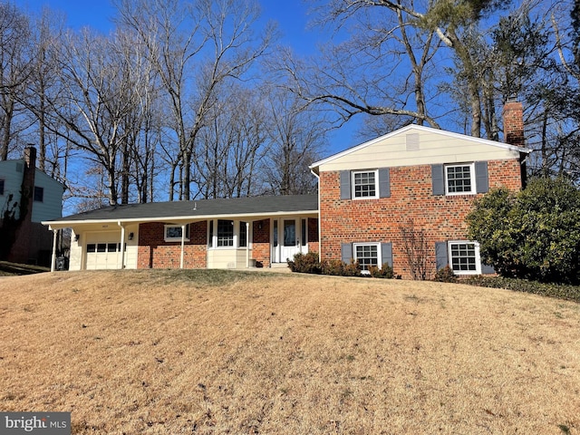 tri-level home featuring a garage, a chimney, covered porch, a front lawn, and brick siding