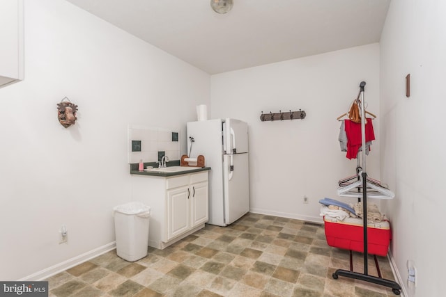 kitchen featuring freestanding refrigerator, white cabinetry, a sink, and baseboards