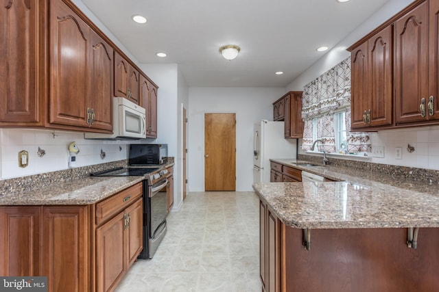 kitchen with a sink, dark stone countertops, white appliances, a peninsula, and a kitchen breakfast bar