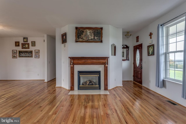 unfurnished living room featuring a fireplace with flush hearth, visible vents, light wood-style flooring, and baseboards