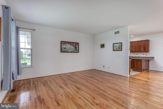 unfurnished living room featuring light wood-type flooring, visible vents, and baseboards