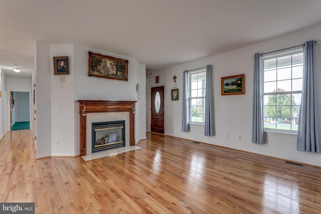 unfurnished living room featuring a fireplace with flush hearth, visible vents, plenty of natural light, and light wood finished floors