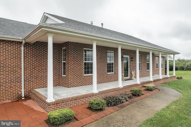 exterior space with covered porch, a shingled roof, and brick siding