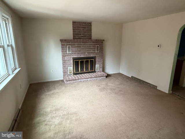 unfurnished living room featuring arched walkways, visible vents, baseboard heating, a brick fireplace, and carpet