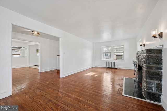 unfurnished living room featuring a stone fireplace, radiator heating unit, wood finished floors, and baseboards