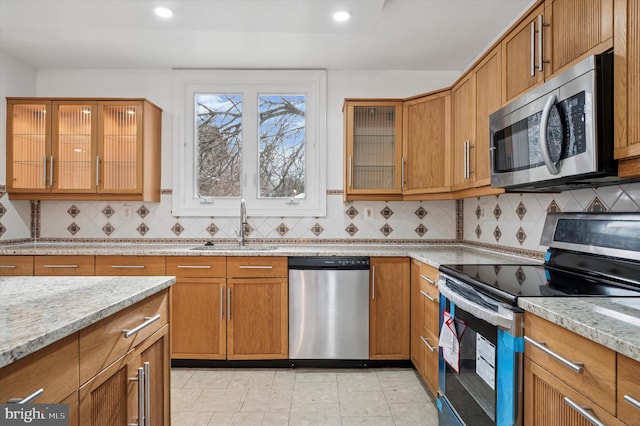 kitchen featuring stainless steel appliances, tasteful backsplash, a sink, and light stone countertops