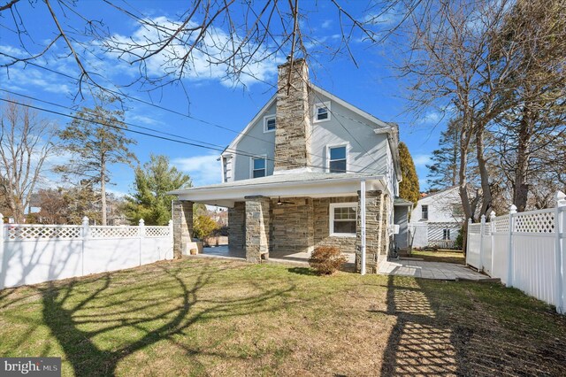 rear view of property featuring a patio, a chimney, a lawn, stone siding, and a fenced backyard