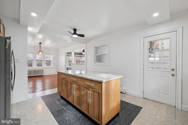 kitchen featuring light stone counters, baseboards, freestanding refrigerator, radiator, and brown cabinetry