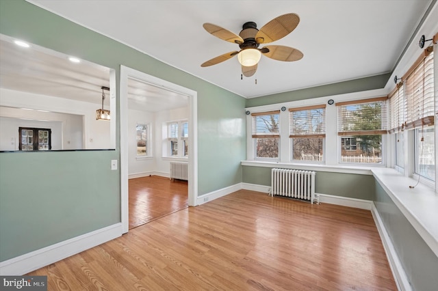 empty room with radiator heating unit, baseboards, ceiling fan, and wood finished floors