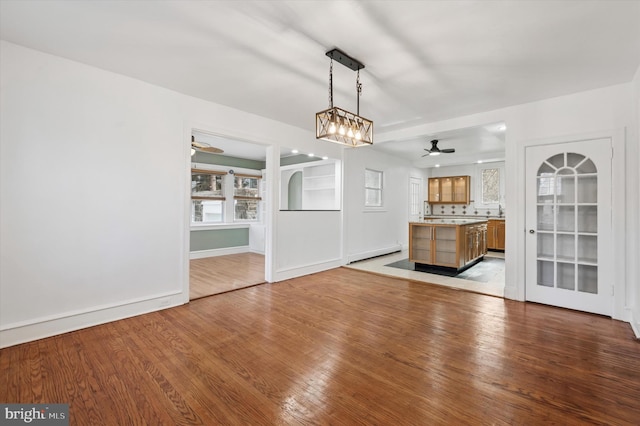 unfurnished living room with ceiling fan, a baseboard radiator, and wood finished floors