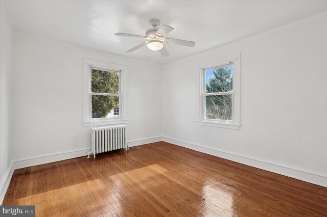 unfurnished room featuring a ceiling fan, radiator, wood-type flooring, and baseboards