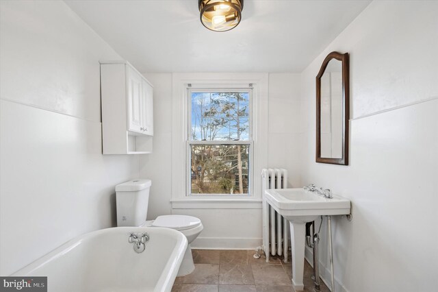 full bath with toilet, radiator heating unit, a sink, a freestanding tub, and baseboards