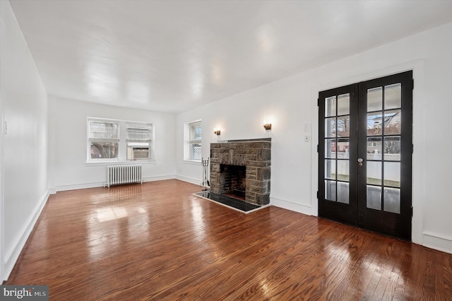 unfurnished living room featuring french doors, radiator, hardwood / wood-style floors, a stone fireplace, and baseboards