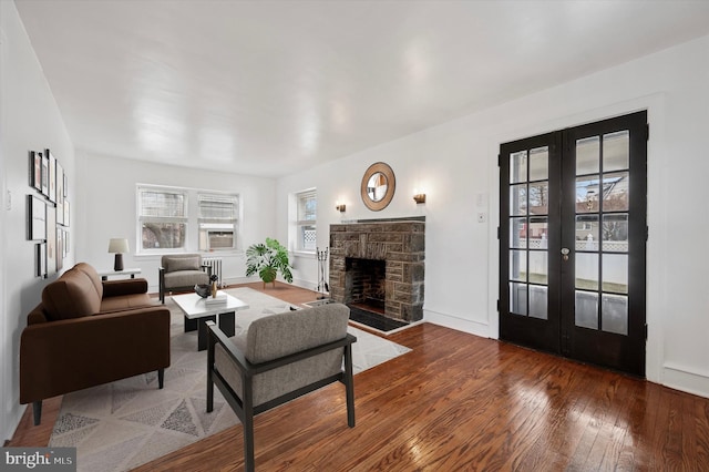 living area featuring french doors, radiator, a stone fireplace, cooling unit, and hardwood / wood-style floors