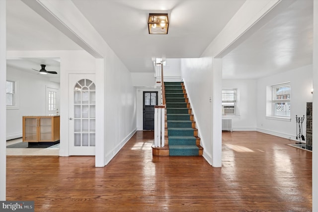 foyer with radiator heating unit, wood finished floors, cooling unit, baseboards, and stairs