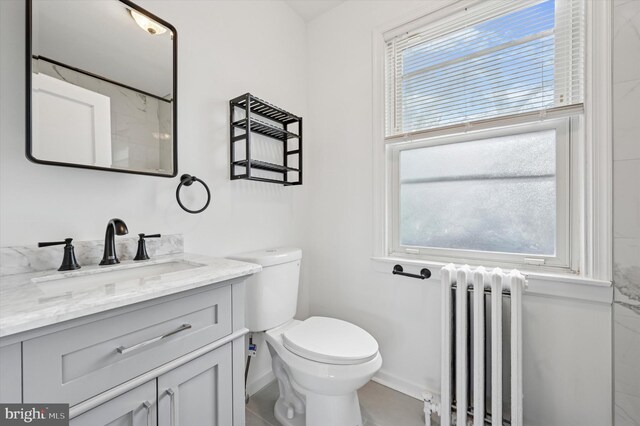 bathroom with toilet, radiator heating unit, vanity, and baseboards