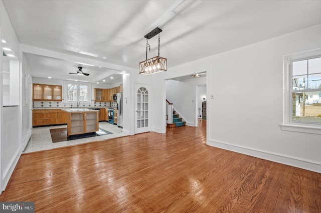 unfurnished living room featuring baseboards, a sink, stairway, and light wood finished floors