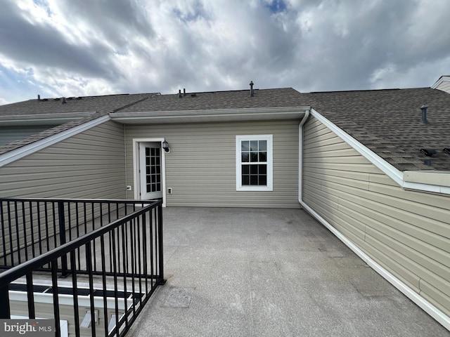 back of property with roof with shingles and a patio