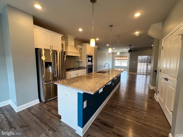 kitchen featuring dark wood finished floors, custom range hood, appliances with stainless steel finishes, a large island with sink, and a sink