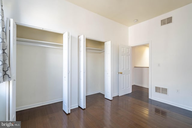 unfurnished bedroom with multiple closets, visible vents, baseboards, and wood finished floors