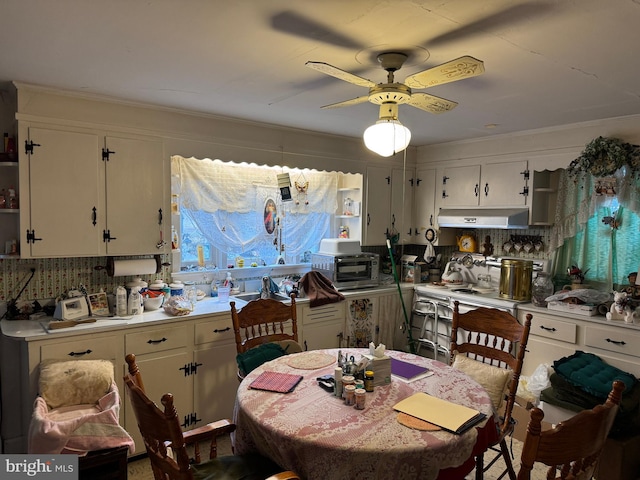 kitchen featuring light countertops, backsplash, white cabinetry, and under cabinet range hood