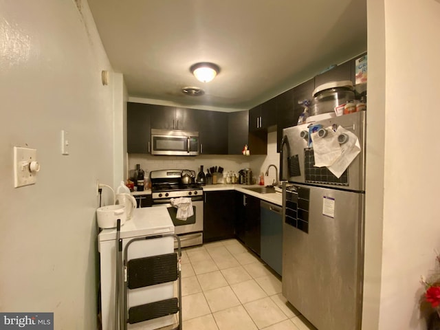 kitchen featuring dark cabinetry, light tile patterned flooring, a sink, light countertops, and appliances with stainless steel finishes